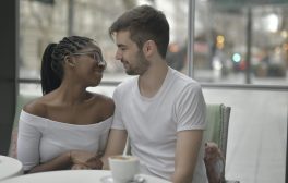 egy fekete hajú nő és egy fehér pólós férfi egy kávézó asztalánál ülnek randevún