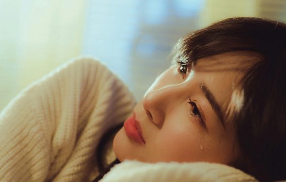 A woman in a sweater lying down and shedding a tear in a warm setting.