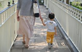 A mother and son holding hands walking on a sunlit cobblestone path.