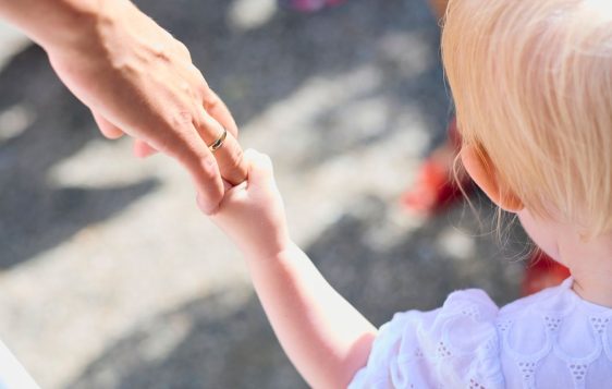 Blonde child holding parent's hand outdoors, symbolizing love and protection.