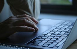 Close-up of a person's hands typing on a laptop keyboard indoors. Soft lighting.