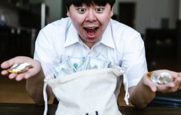 Asian man excitedly holding cryptocurrency and US dollars, symbolizing financial success and wealth.
