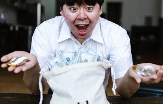 Asian man excitedly holding cryptocurrency and US dollars, symbolizing financial success and wealth.