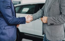 Two businessmen shaking hands in a car dealership, sealing a deal.