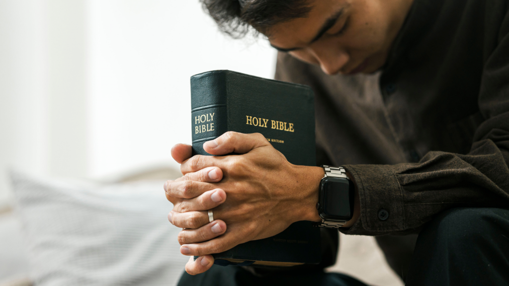 mężczyzna modlący się z z zamkniętymi oczami i trzymający Biblię