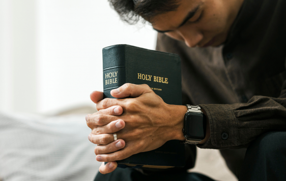 mężczyzna modlący się z z zamkniętymi oczami i trzymający Biblię